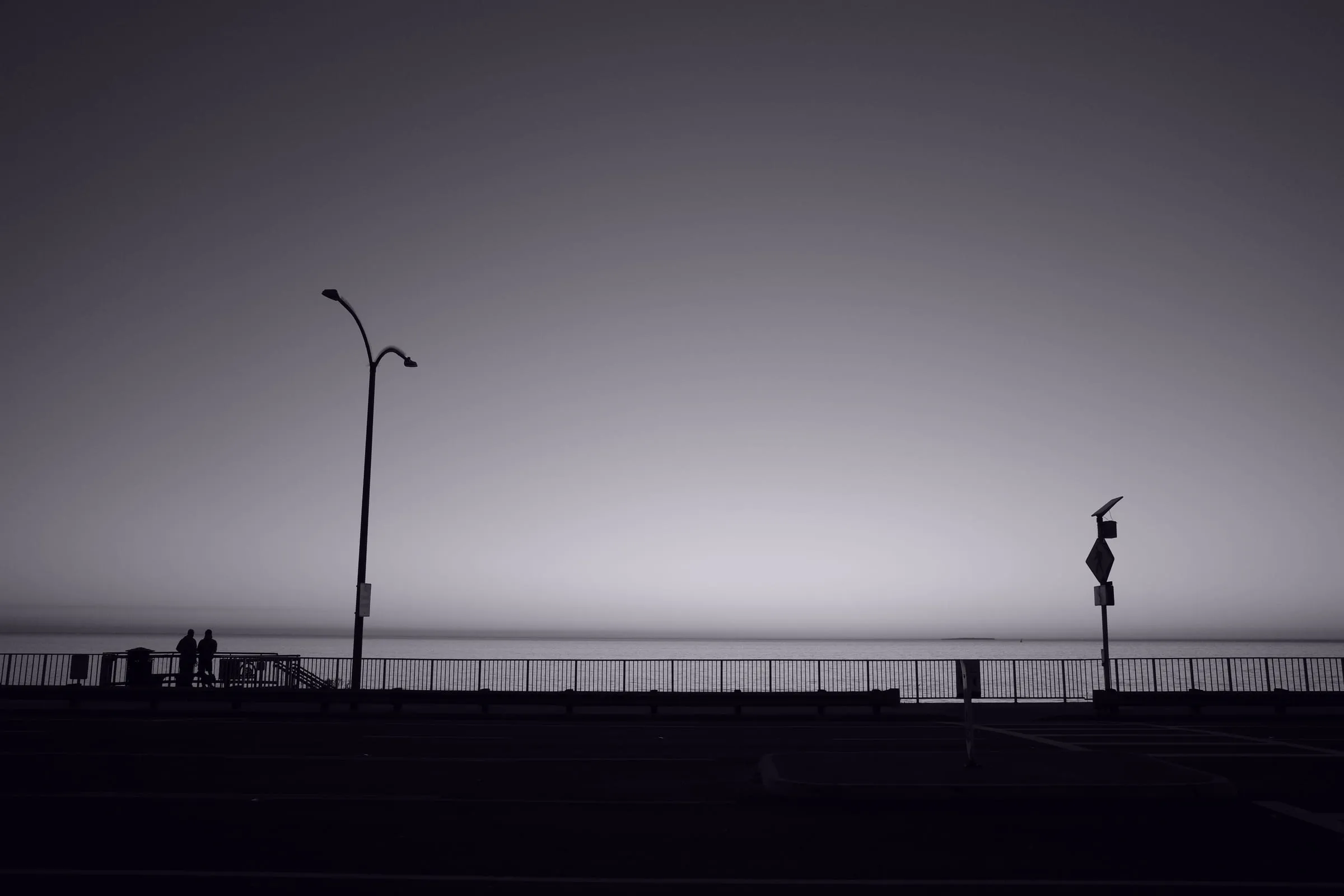 Dusk on the coast road — streetlamp and railing silhouetted against a fading sky over the Pacific